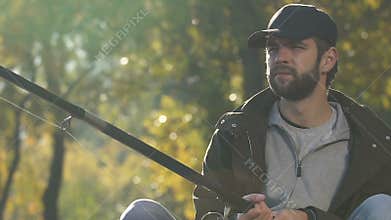 Bored male spinning fishing reel to check bait near river, bad day, poor catch