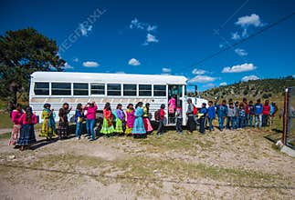 Indigenous school students in traditional colorful dress with a school bus, Mexico, America