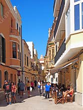 Tourists and shoppers walking and sitting in an outdoor cafe in the street in Ciutadella Menorca town center