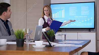 In conference room businesswoman with a clipboard in hands presents company data