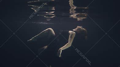 Young woman in black dress swimming underwater in pool while video shooting