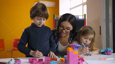 Teacher helping class of preschool kids to draw