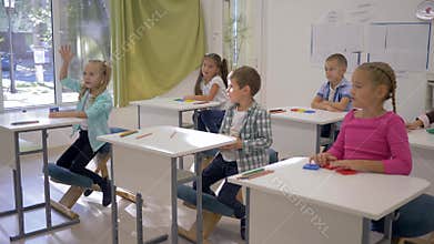 Children at school, boys and girls sit at desks and raise hands during lesson in classroom in school