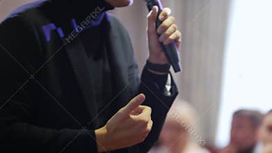 A man talking on the stage giving a lecture to the audience holding a microphone