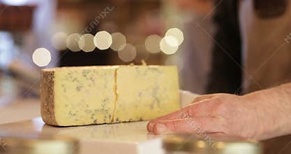 Male sales assistant in delicatessen cutting slice of cheese