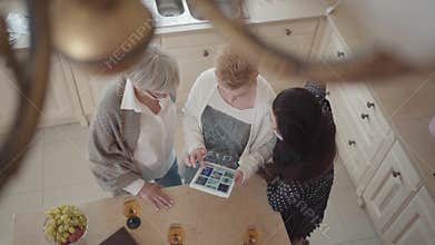 Senior woman showing to her friends photos on tablet. Group of three middle aged mature women communicating chatting
