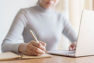 Asian woman is taking notes and using  laptop computer at office