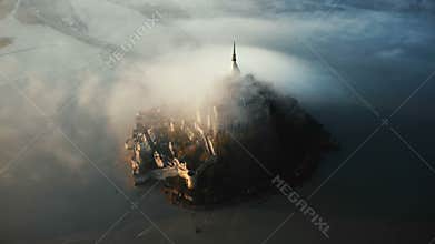 Drone flying high around amazing Mont Saint Michel island castle fortress covered with massive sunrise fog clouds flow.