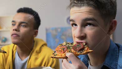 Two male teenagers watching tv and eating pizza, fatty cheap snacks, fast food