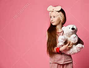 Smiling baby girl holding a white teddy bear in the room a pink backdrop.