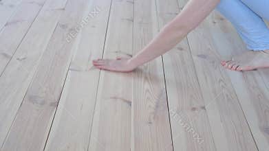 Eco-friendly flooring - woman with bare feet strokes the warm wooden floor closeup.