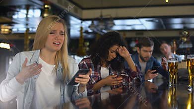 Young women in bar checking sport bets in cellphone, upset about lost money