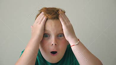 Young kid clutches his head showing joy and delight on face. Adorable boy looks into camera with emotions and feelings