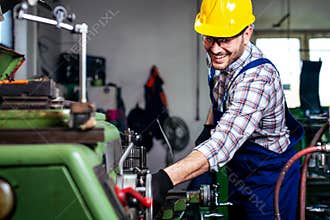 Metal worker turner operating lathe machine at industrial manufacturing factory.