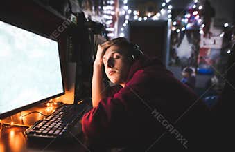 Portrait of a young gamer with headphones, plays games at night on the computer, and falls asleep on the table