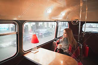 Young attractive woman sitting at the table in the bus cafe is covered with a blanket