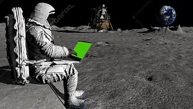 Astronaut on the moon typing on a laptop with a green screen.