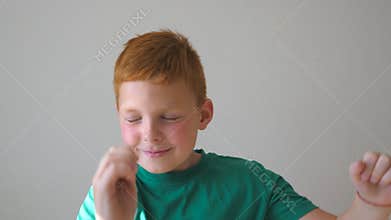Handsome cute kid dancing with raising hands indoor. Happy male child closing his eyes and enjoy to rejoicing