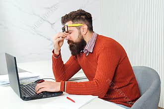 Tired man with laptop computer at working place. Bearded man overworked at office. Stressed handsome business man. Feeling