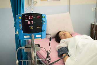 Focus on blood pressure monitor with patient on bed in hospital ward. Medical concept