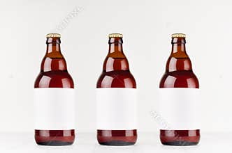 Three brown belgian steinie beer bottles 500ml with blank white label on white wooden board, mock up.