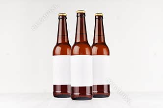 Three brown longneck beer bottles 500ml with blank white label on white wooden board, mock up.