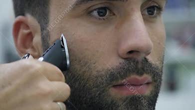 Hairstyling process. Close-up of a barber drying hair of a young bearded man