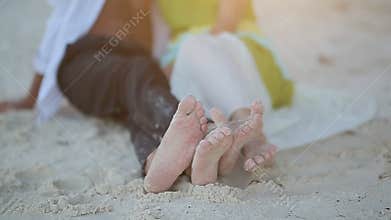 Love couple lying on the sand and their bare feet. Love game of feet. The ray of the sun at sunset slips in the frame.