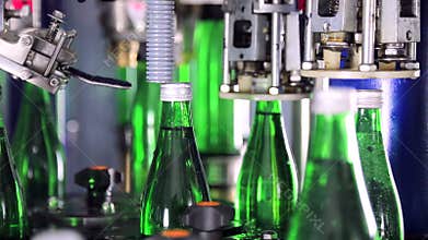 Automatically covering bottles with lids in water plant. Green glass bottles on automatic conveyor line.