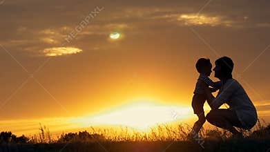A silhouette of a happy young boy child running into the arms of his loving mother for a hug, in front of the sunset in