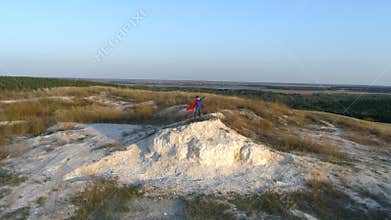 A boy dressed up with a Cape of Superman standing on a mountain looking at the sunset