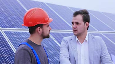 Businessman talking to a worker on a background of solar panels