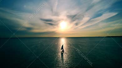 Little white boat floating on the water towards the horizon in the rays of the setting sun. Beautiful clouds with yellow highlight