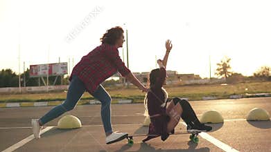 Side view of a woman with her hands raised up sitting on a longboard while her friend is pushing her behind and running