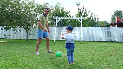 Dad with a four-year-old son playing ball, football, in the yard on a green lawn, in the summer.