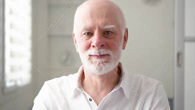 Portrait of handsome bearded senior man at home. Sitting in living room looking at camera