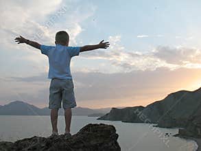 Boy stand on mountain top with hands up
