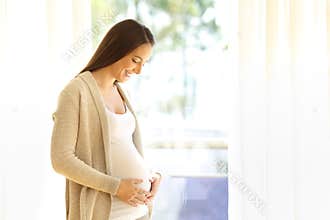 Pregnant mother looking at her belly at home