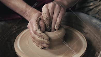 The hands of a potter, creating an earthen jar on the circle, close-up, hands on circle with clay