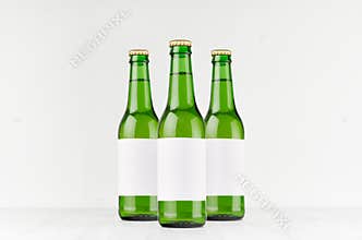 Three green longneck beer bottles 330ml with blank white label on white wooden board, mock up.