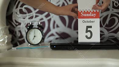 The girl opens a new calendar sheet. October 4, Saturday changes on October 5 Sunday. Day off. A calendar, a laptop, an