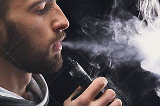 Young man vaping e-cigarette with smoke on black
