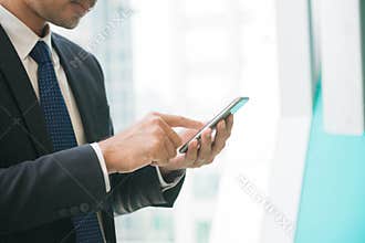 Businessman using mobile phone app texting outside of office in urban city with skyscrapers buildings in the background.