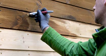 Worker painting house exterior with wood protective color