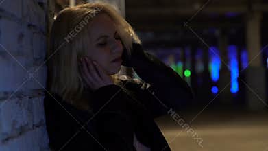 Frustrated blond woman suffering from headache, standing alone outside nightclub