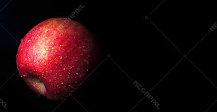 Water droplet on glossy surface of red apple on black background