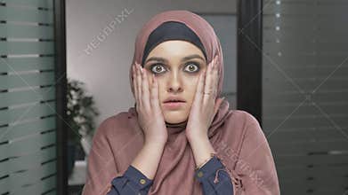 A young Arab girl in red hijab is surprised, shows an emotion of surprise. Looks at the camera, portrait. 60 fps