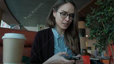 Cute Caucasian girl brunette holding cellular phone in her hands with an upset, irritated look.