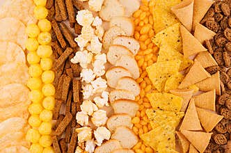 Assortment crunchy snacks - popcorn, nachos, croutons, corn sticks, potato chips as decorative background, top view, closeup.