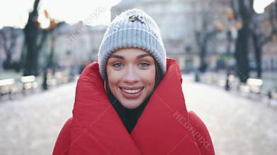 Portrait of a stunning girl in grey hat and red coat smiling while she stands on the street before Christmas decorations
